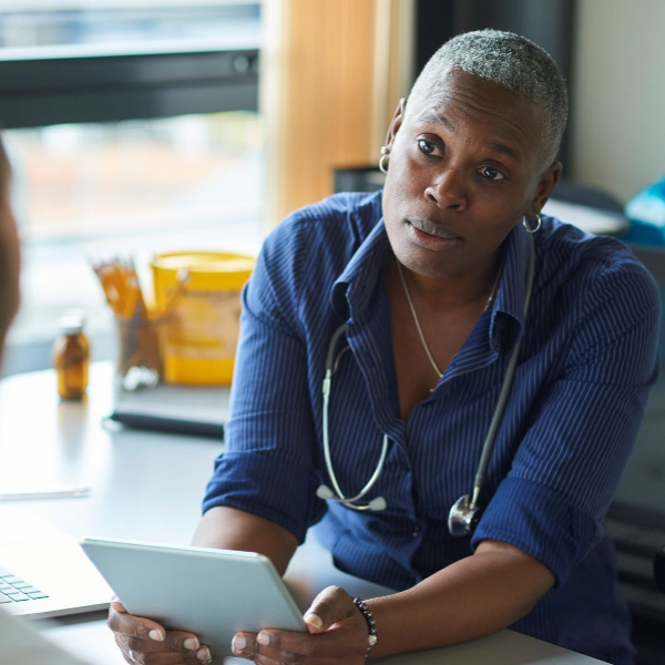 Female healthcare professional with stethoscope around her heck listening intently to a patient while holding a tablet
