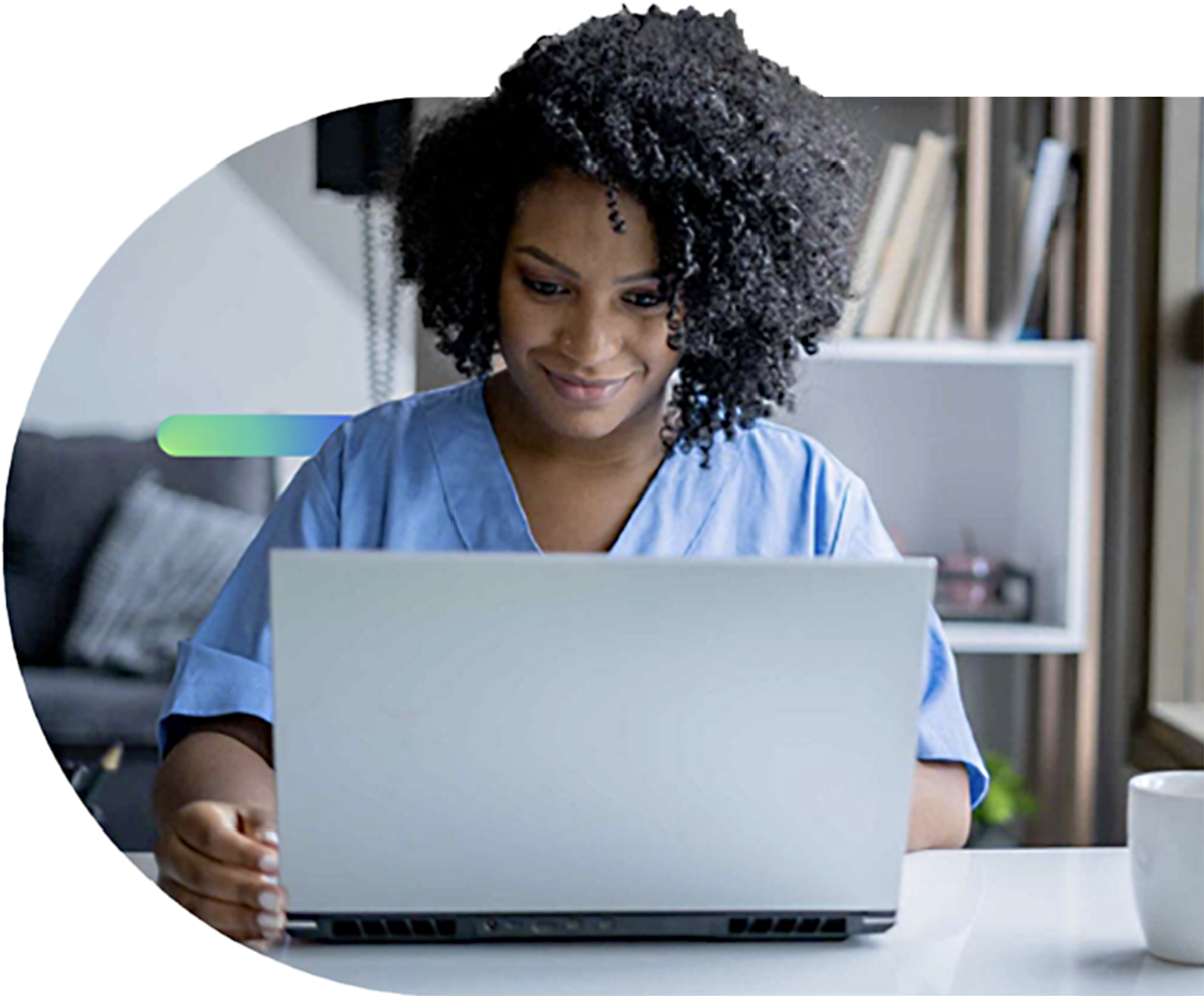 Nurse in blue scrubs smiling while reviewing a patient file on a laptop