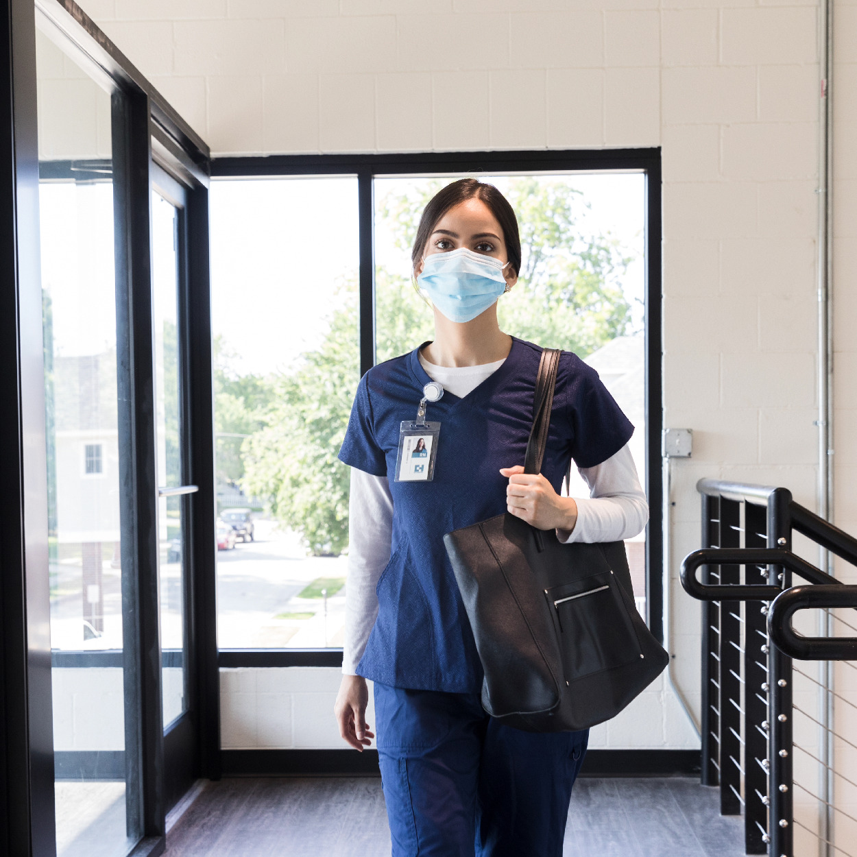 Female nurse in navy scrubs with mask walking into a shift