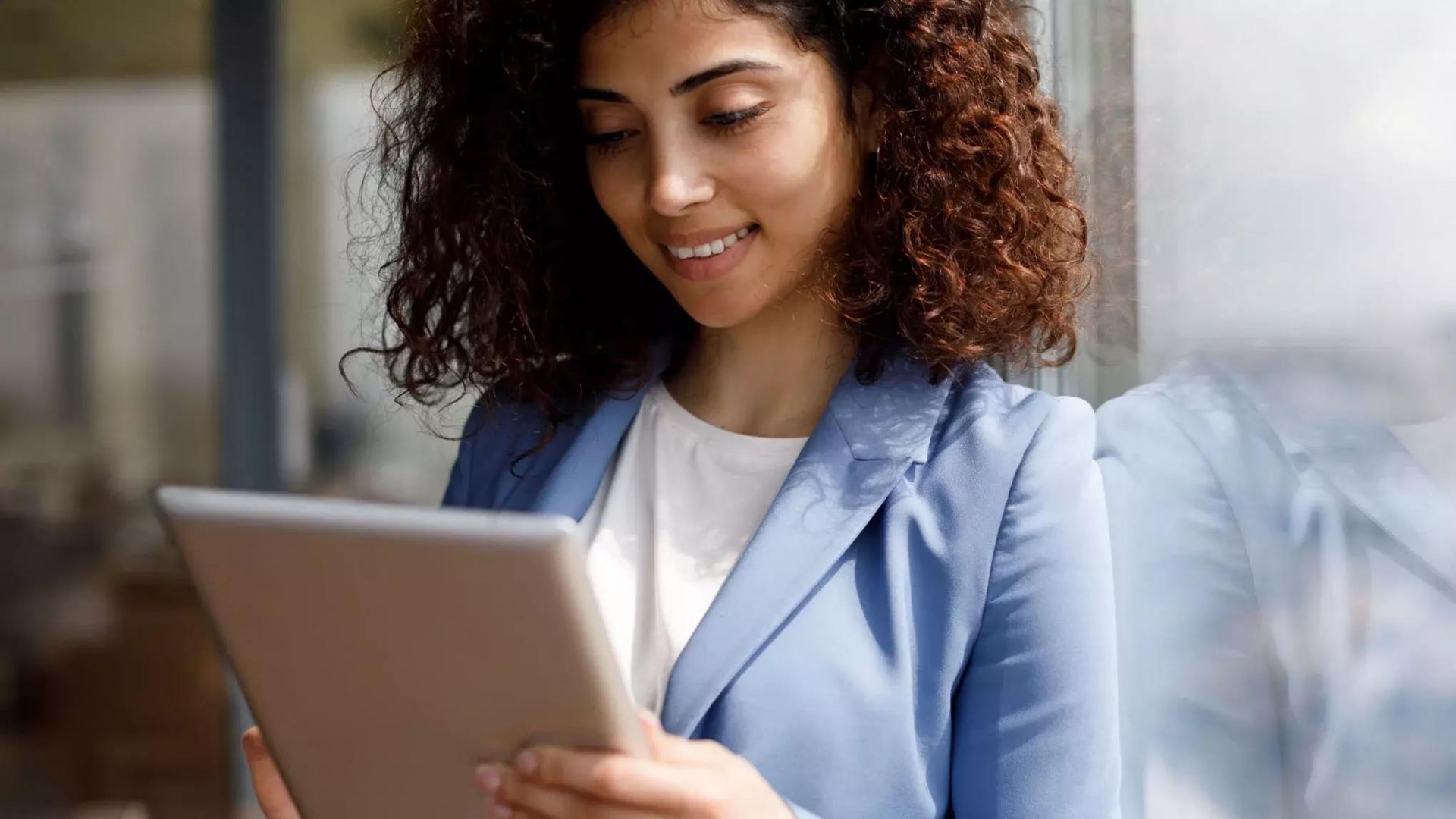 Woman in light blue blazer smiling behind a tablet