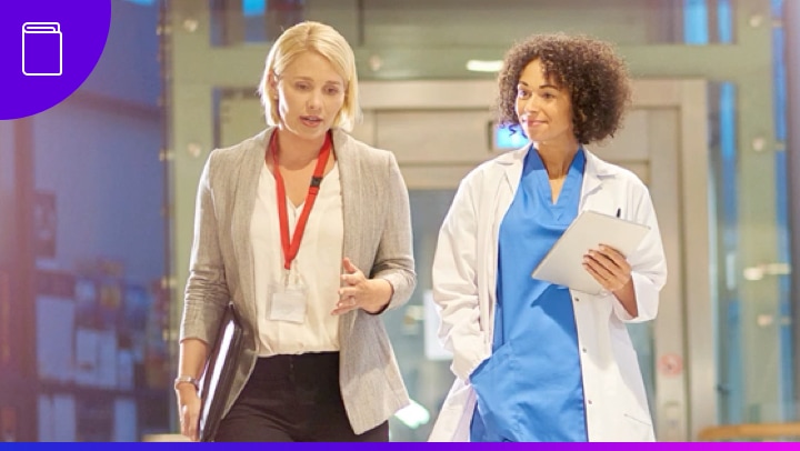 Thumbnail of a healthcare professional and business professional walking and talking down a hospital hallway