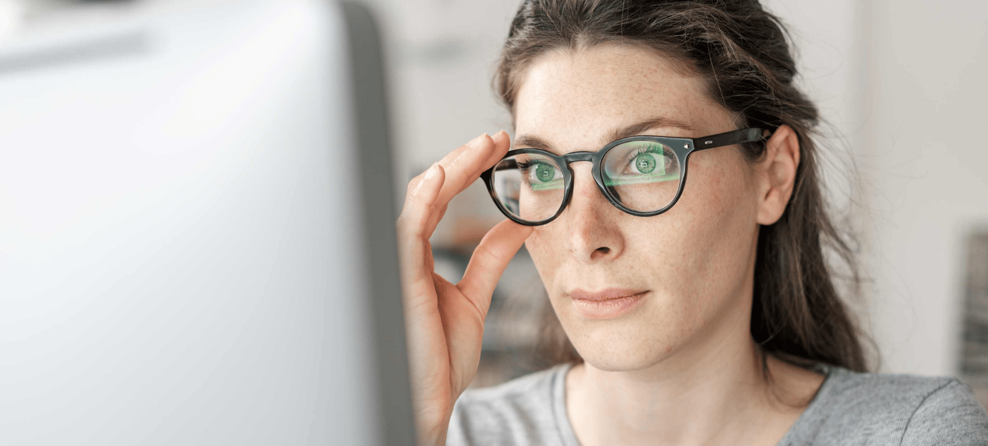 Woman staring at computer screen with hands on her glasses