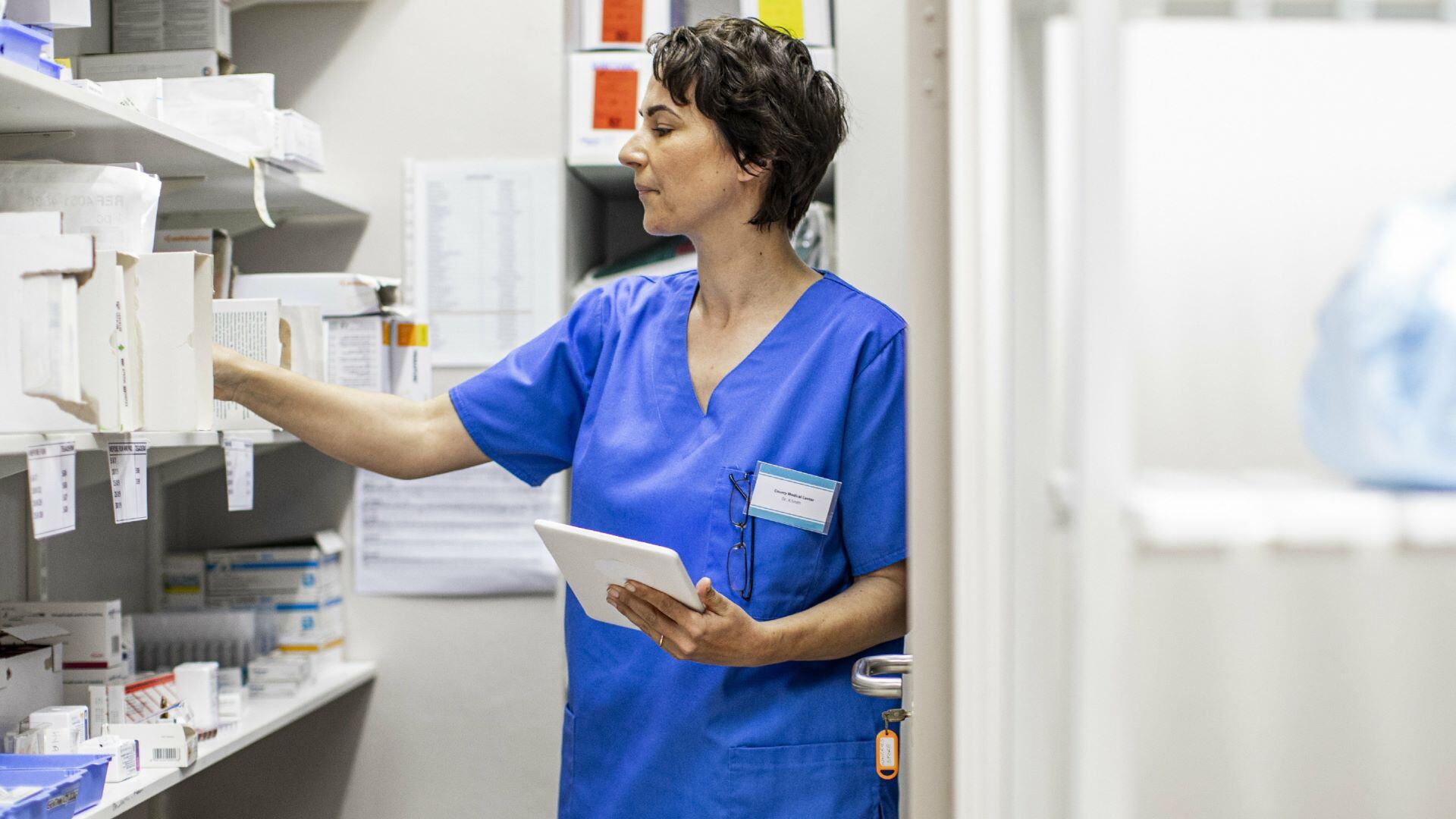 Healthcare worker holding tablet grabbing paper off shelf